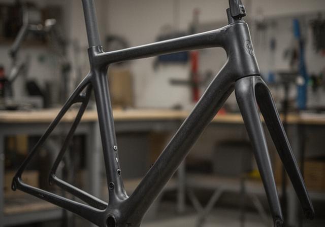 Cuadro de bicicleta de gravel de fibra de carbono colgado en taller con acabado limpio y detalles de unión visibles